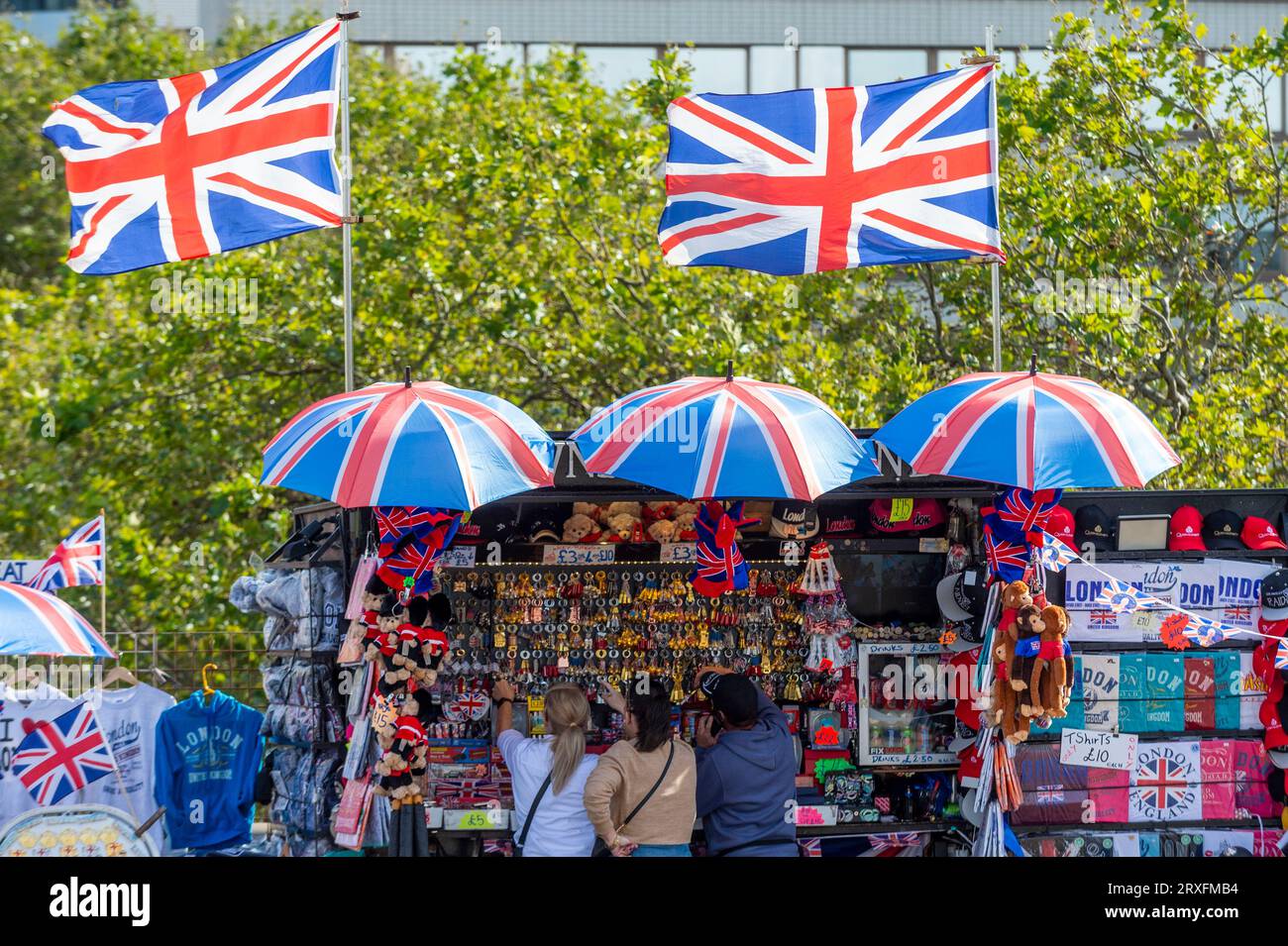 London, UK.  25 September 2023.  UK Weather : Tourists in front of Union Jack flags fluttering in the breeze atop a souvenir stand on Westminster Bridge in the sunshine and temperatures of 22C.  The autumnal equinox occurred two days ago meaning that days will be shorter and nights longer.  Credit: Stephen Chung / Alamy Live News Stock Photo