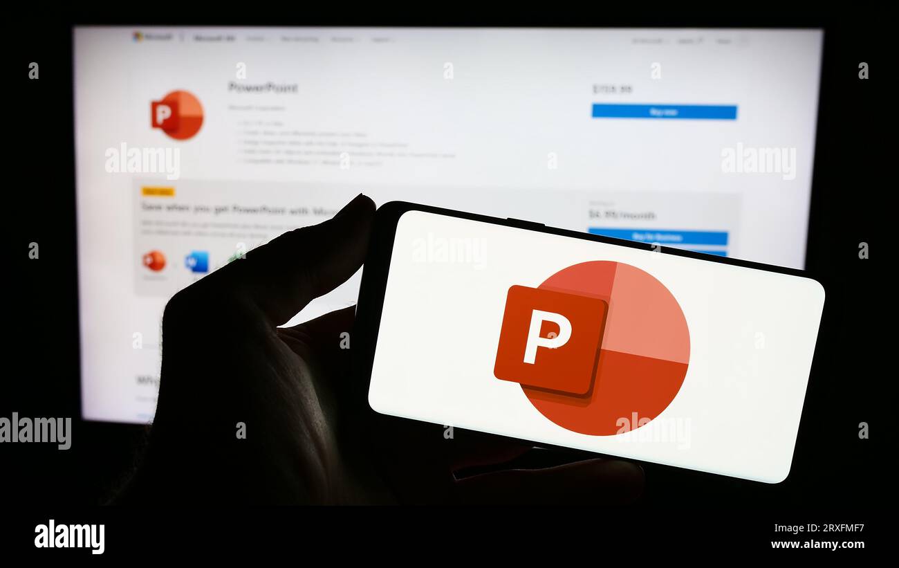 Person holding smartphone with logo of presentation software Microsoft PowerPoint on screen in front of website. Focus on phone display. Stock Photo