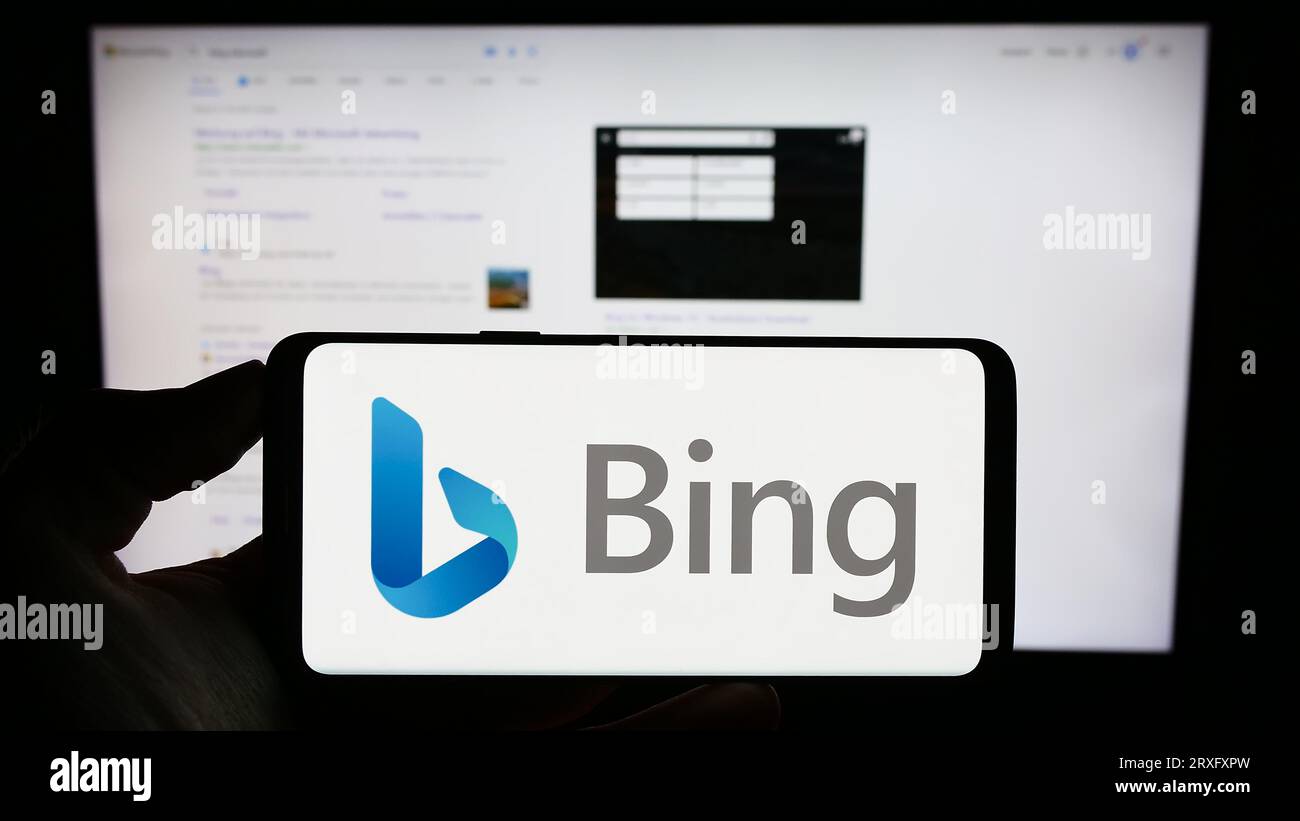 Person holding cellphone with logo of web search engine Microsoft Bing on screen in front of business webpage. Focus on phone display. Stock Photo