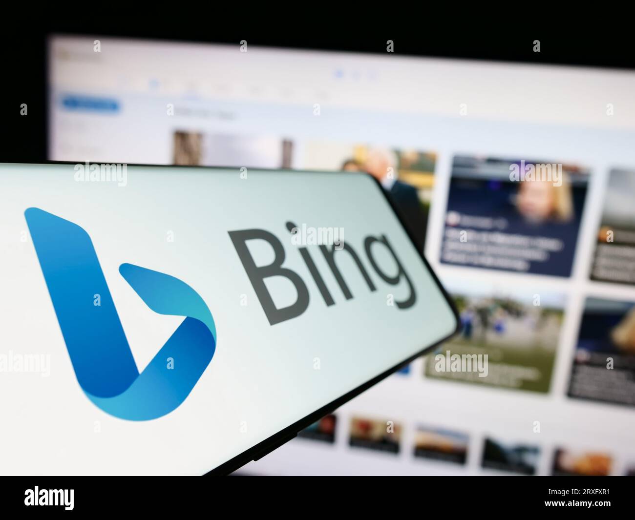 Mobile phone with logo of web search engine Microsoft Bing on screen in front of business website. Focus on center-left of phone display. Stock Photo