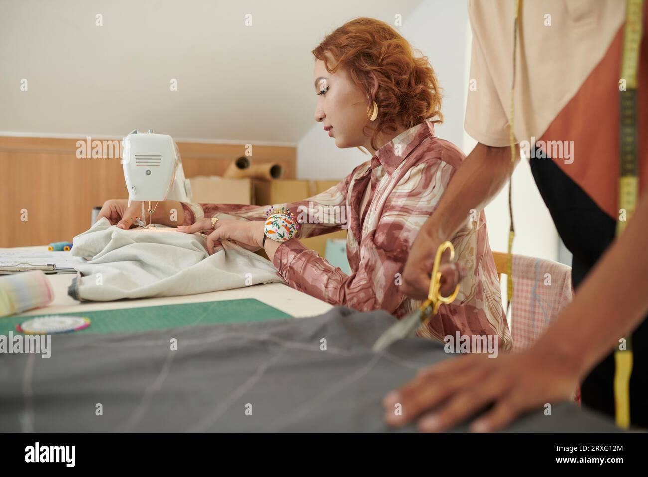 Creative young woman using sewing machine when making gown for client Stock Photo