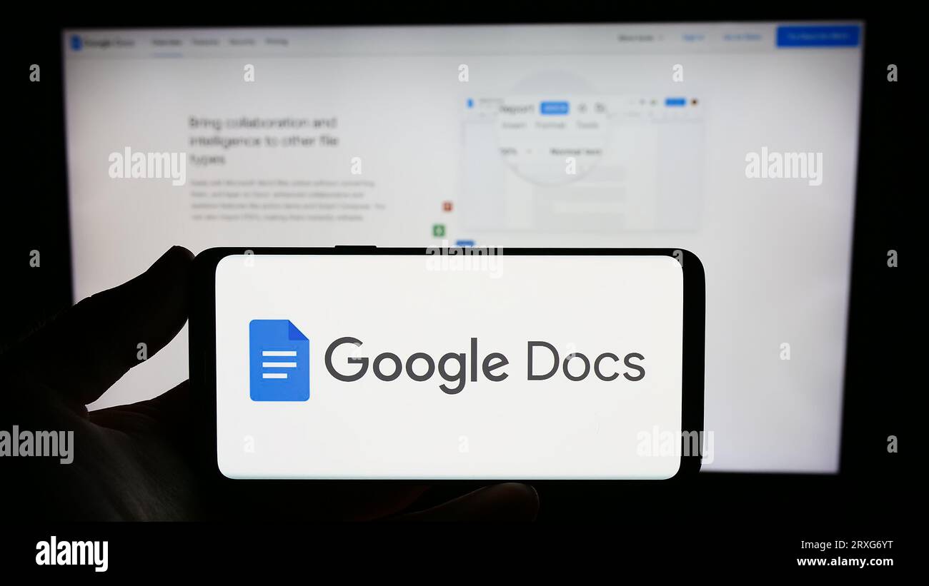 Person holding smartphone with logo of online word processing product Google Docs on screen in front of website. Focus on phone display. Stock Photo