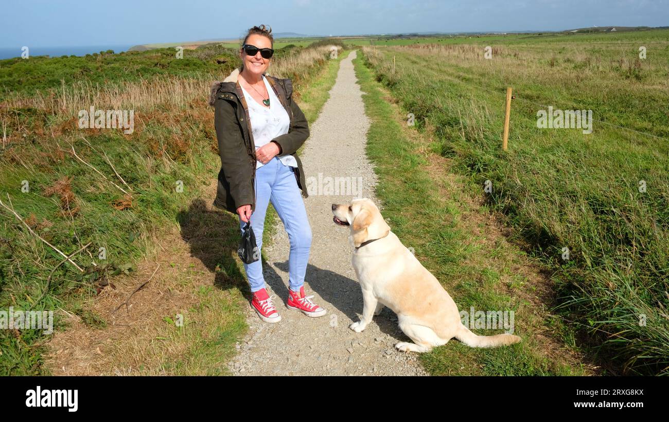 Responsible dog walker holding a poo bag out walking with her labrador - John Gollop Stock Photo