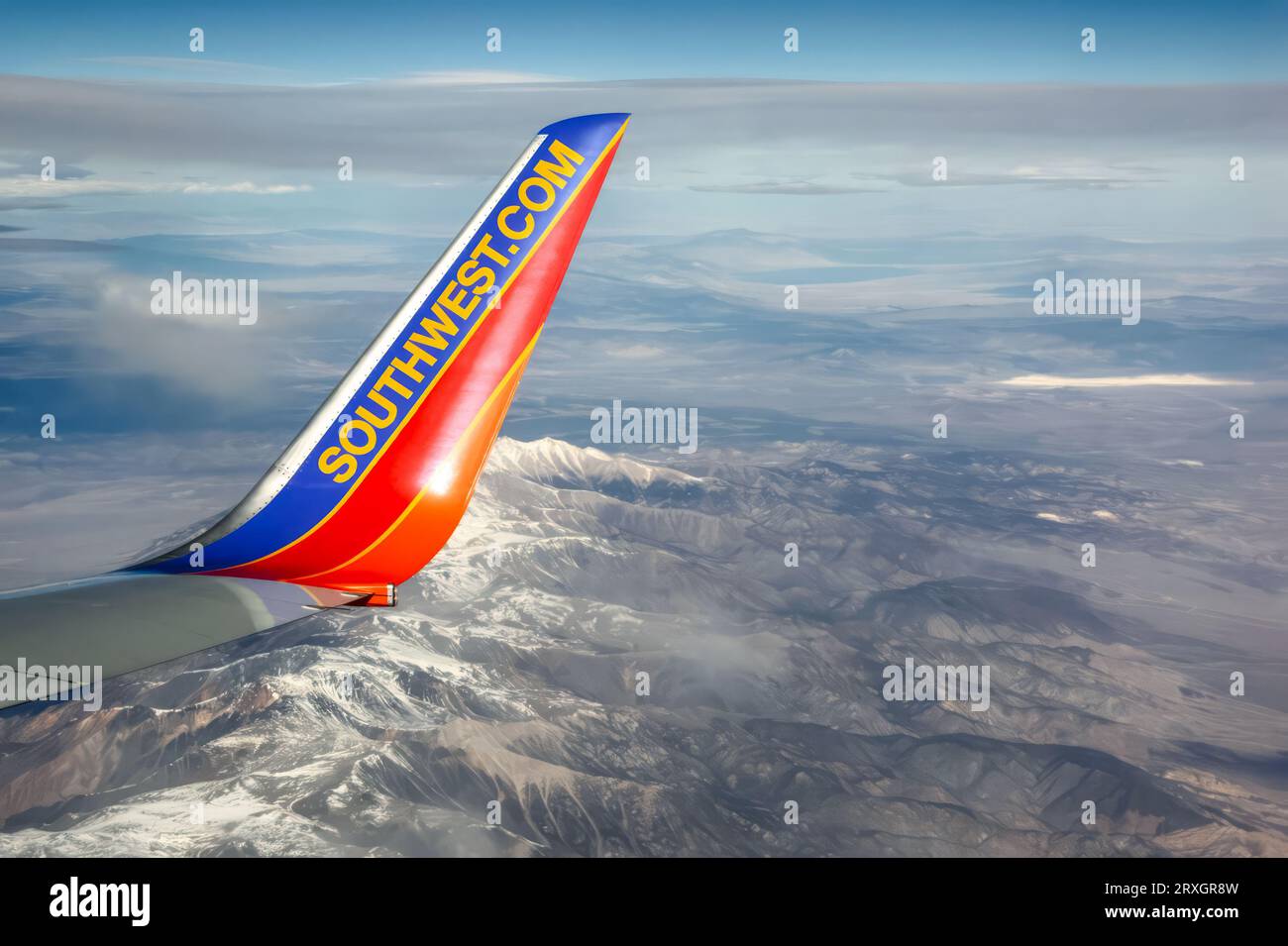 A wing tip of Southwest Airlines Boeing 737 flying over snow-capped mountains. The blue and orange colors contrast with snowy peaks and clear sky. The image captures Southwest's spirit of adventure. Stock Photo