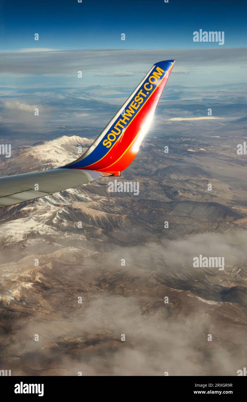 A wing tip of Southwest Airlines Boeing 737 flying over snow-capped mountains. The blue and orange colors contrast with snowy peaks and clear sky. The image captures Southwest's spirit of adventure. Stock Photo