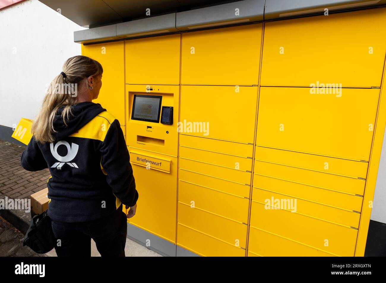 25 September 2023, Saxony, Meißen: A Deutsche Post AG postwoman stands holding a parcel (returns) at a postal station in Meißen, Saxony. In addition to parcels, letters can also be posted at this location. Photo: Daniel Schäfer/dpa Stock Photo