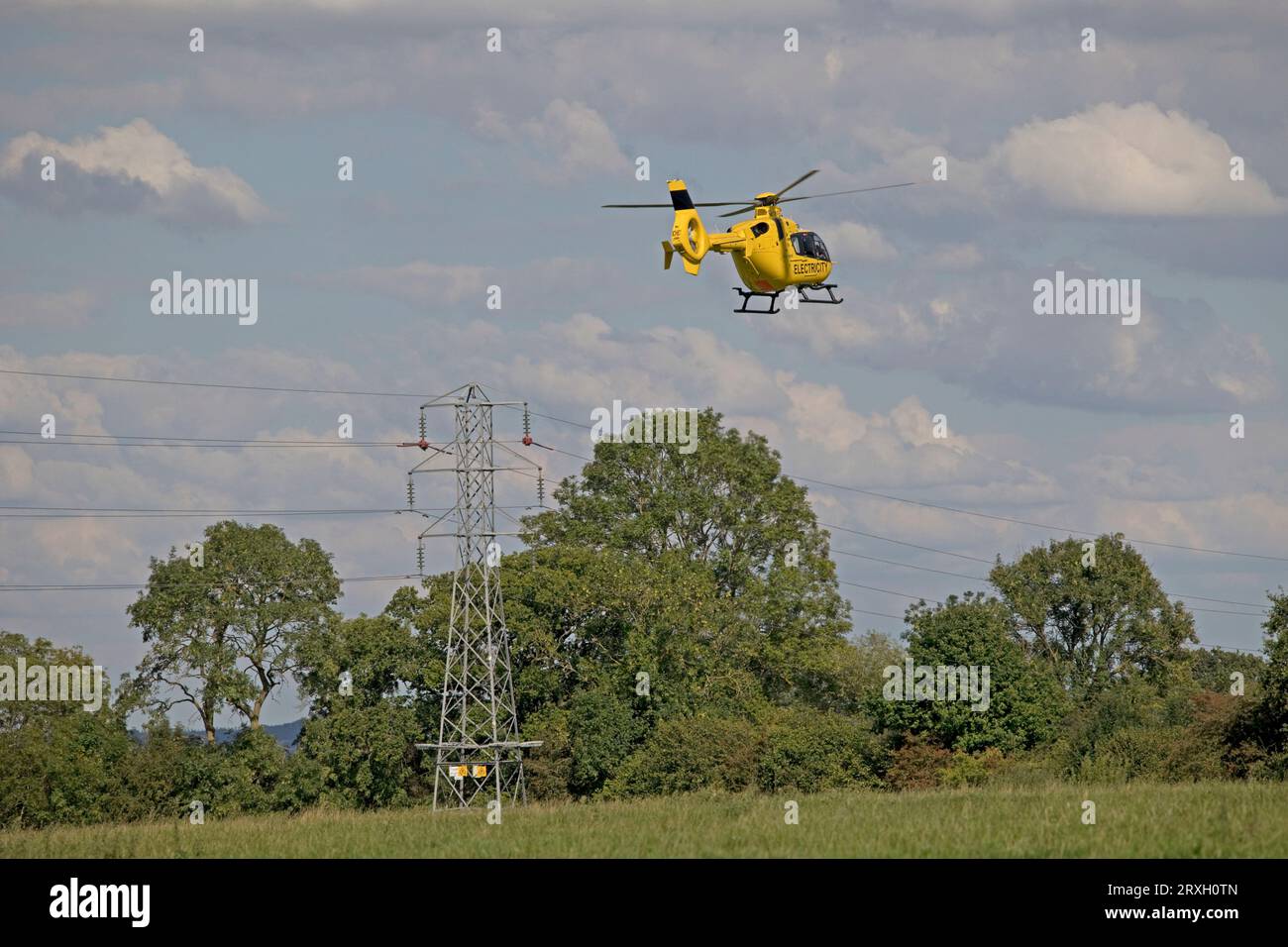 Bright yellow National Grid Electricity helicopter in flight checking high voltage power lines near Mickleton Chipping Campden UK Stock Photo