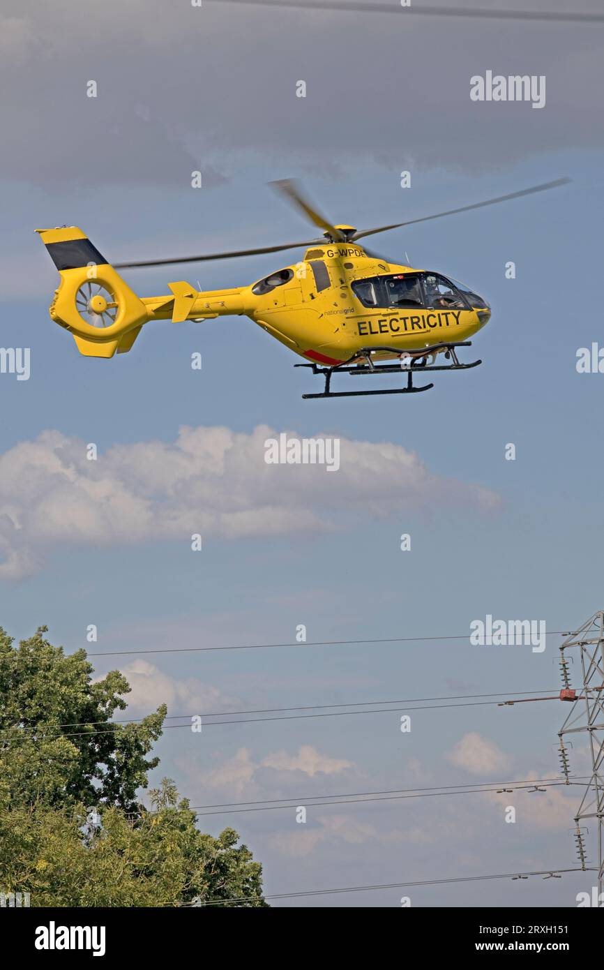 Bright yellow National Grid Electricity helicopter in flight checking high voltage power lines near Mickleton Chipping Campden UK Stock Photo