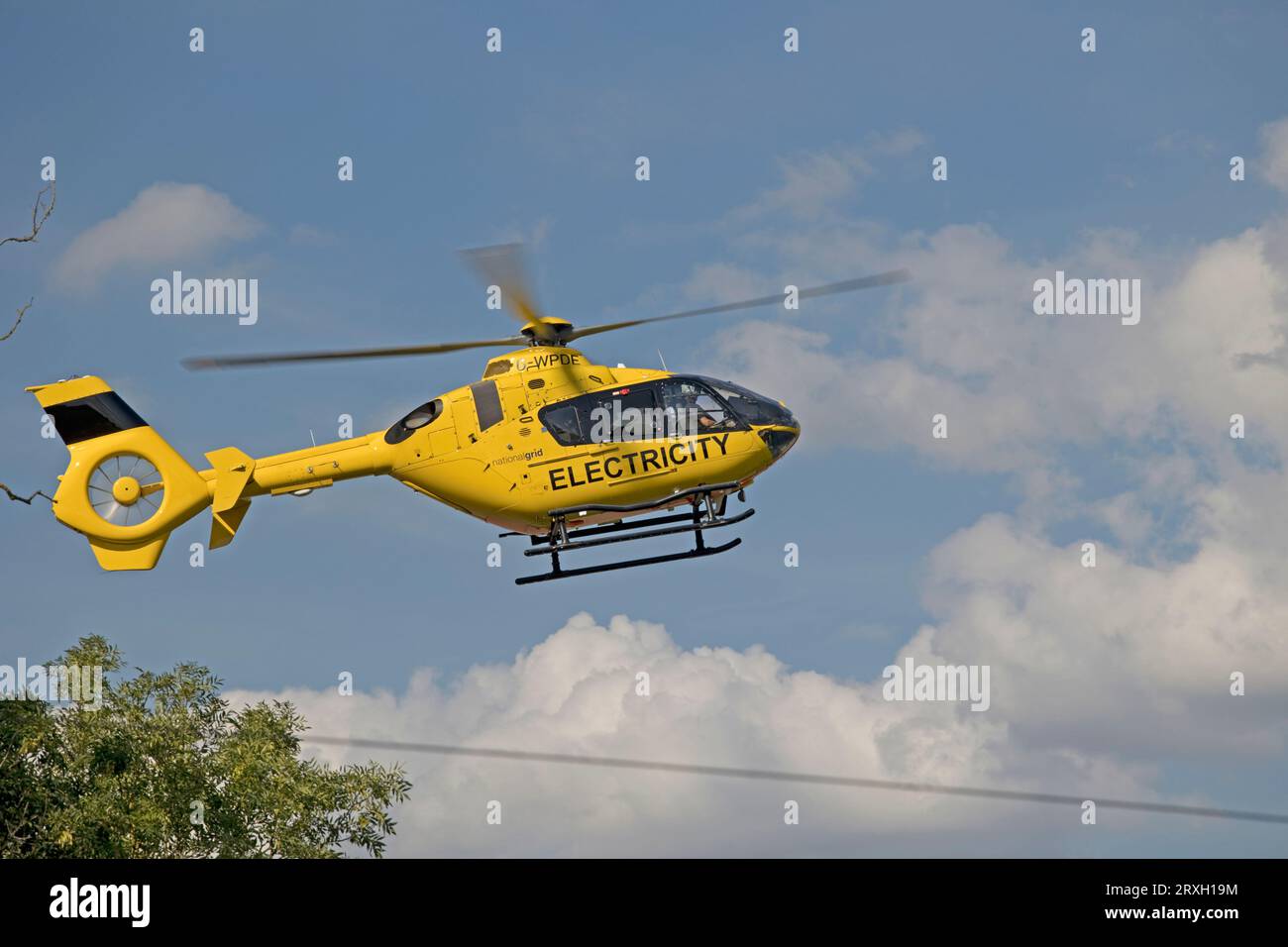 Bright yellow National Grid Electricity helicopter in flight checking high voltage power lines near Mickleton Chipping Campden UK Stock Photo