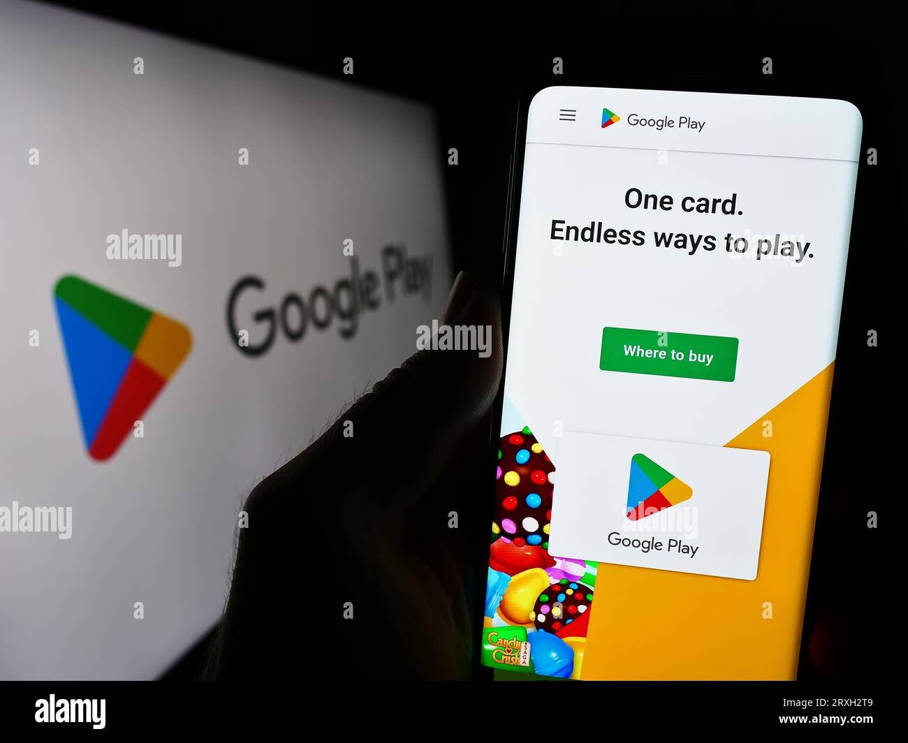 Person holding cellphone with website of app distribution platform Google Play on screen in front of logo. Focus on center of phone display. Stock Photo