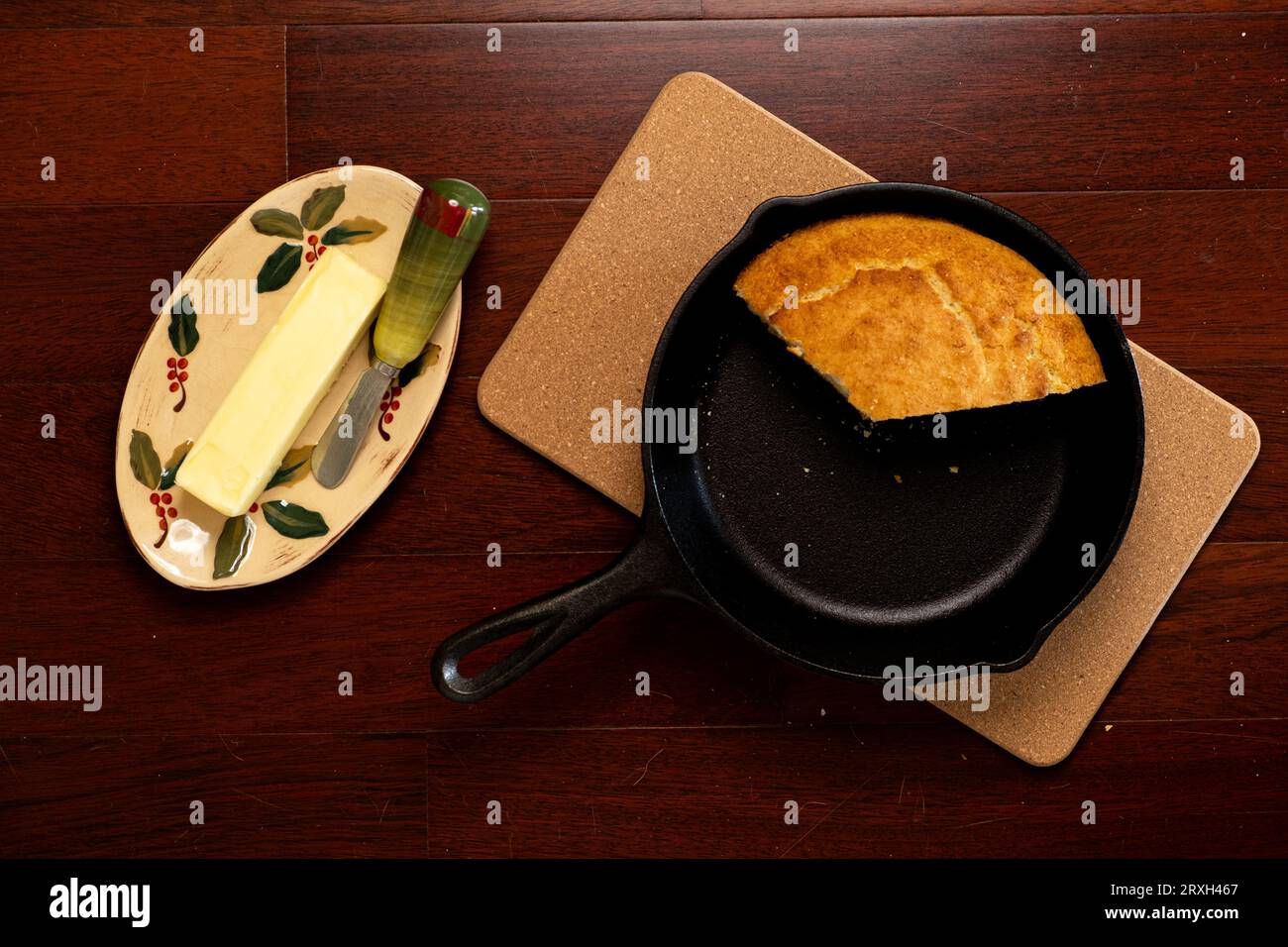 Flat lay of black cast iron skillet with cornbread resting on trivet hot pad with butter dish and knife on side Stock Photo