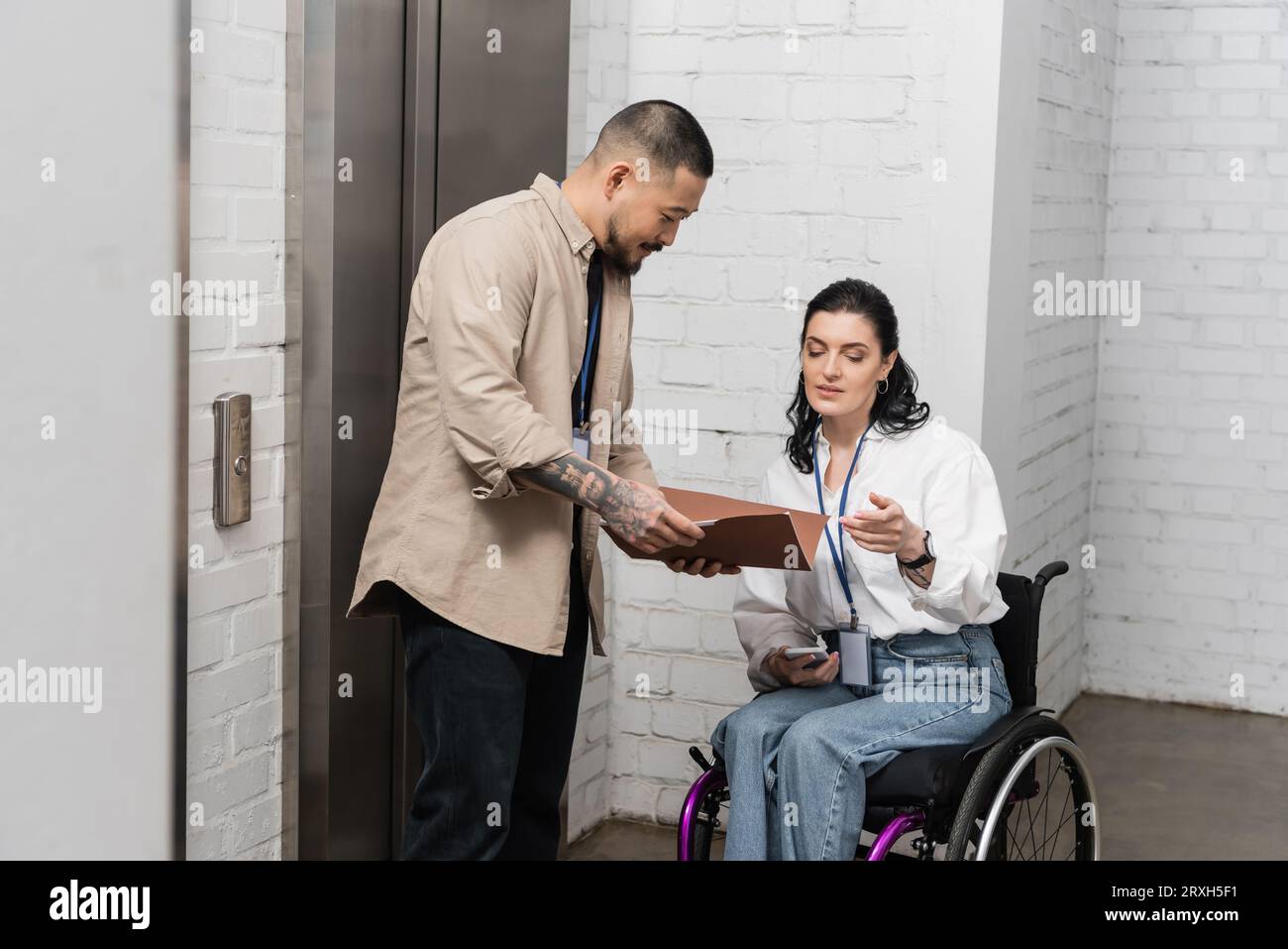 inclusion, asian businessman discussing startup plan with disabled woman near office elevators Stock Photo