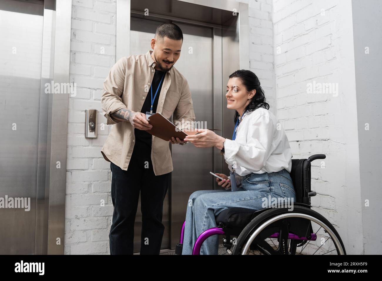 inclusion and diversity, asian man showing startup plan to disabled woman near office elevators Stock Photo