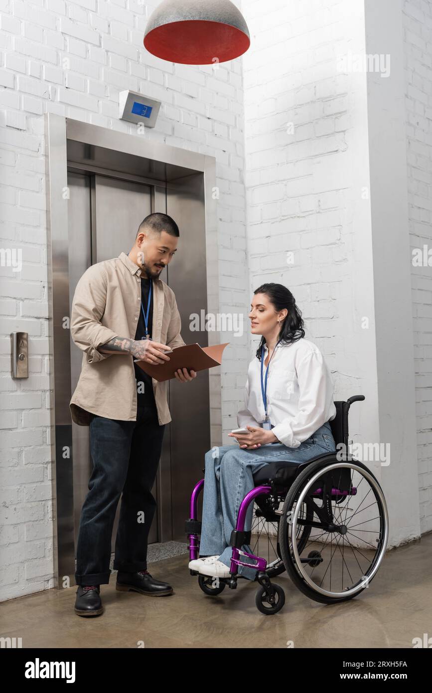 inclusion and diversity, asian man holding startup plan near disabled woman and office elevators Stock Photo