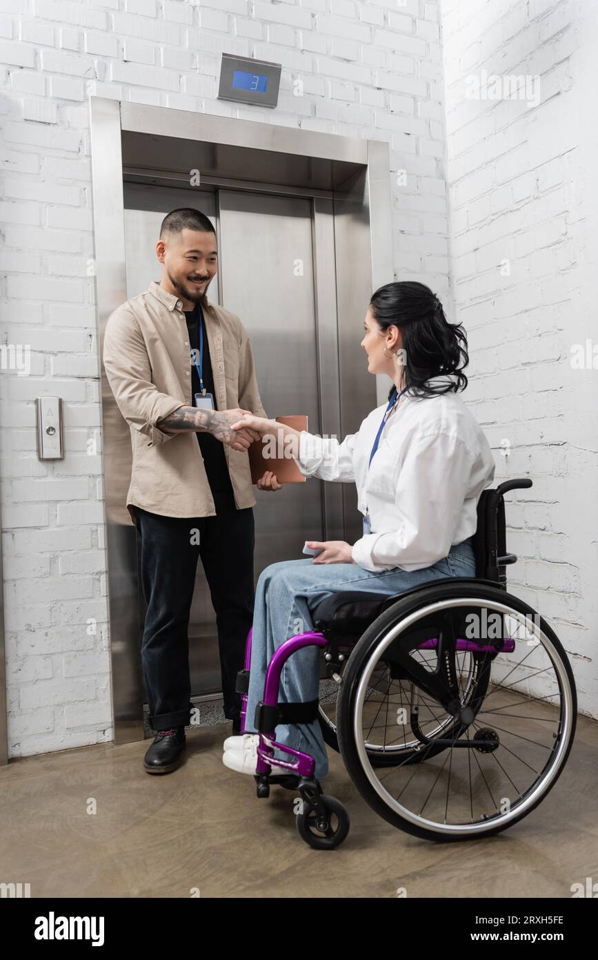 inclusion and diversity, happy asian man shaking hands with disabled woman near office elevators Stock Photo
