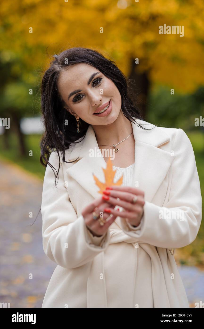 Brunette girl in a white coat in an autumn park Stock Photo