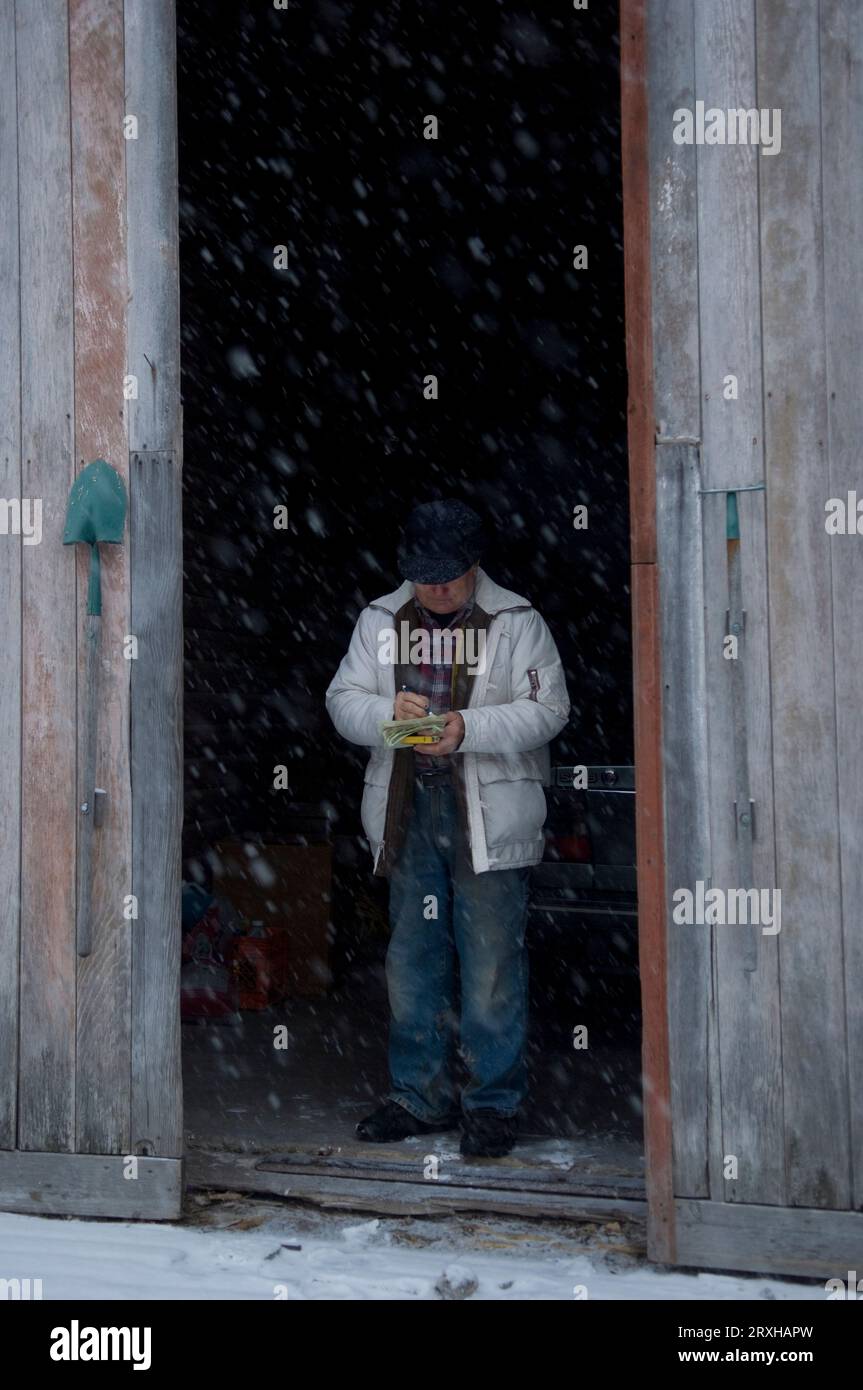 Farmer stands inside a barn doorway in a snowfall; Walton, Nebraska, United States of America Stock Photo