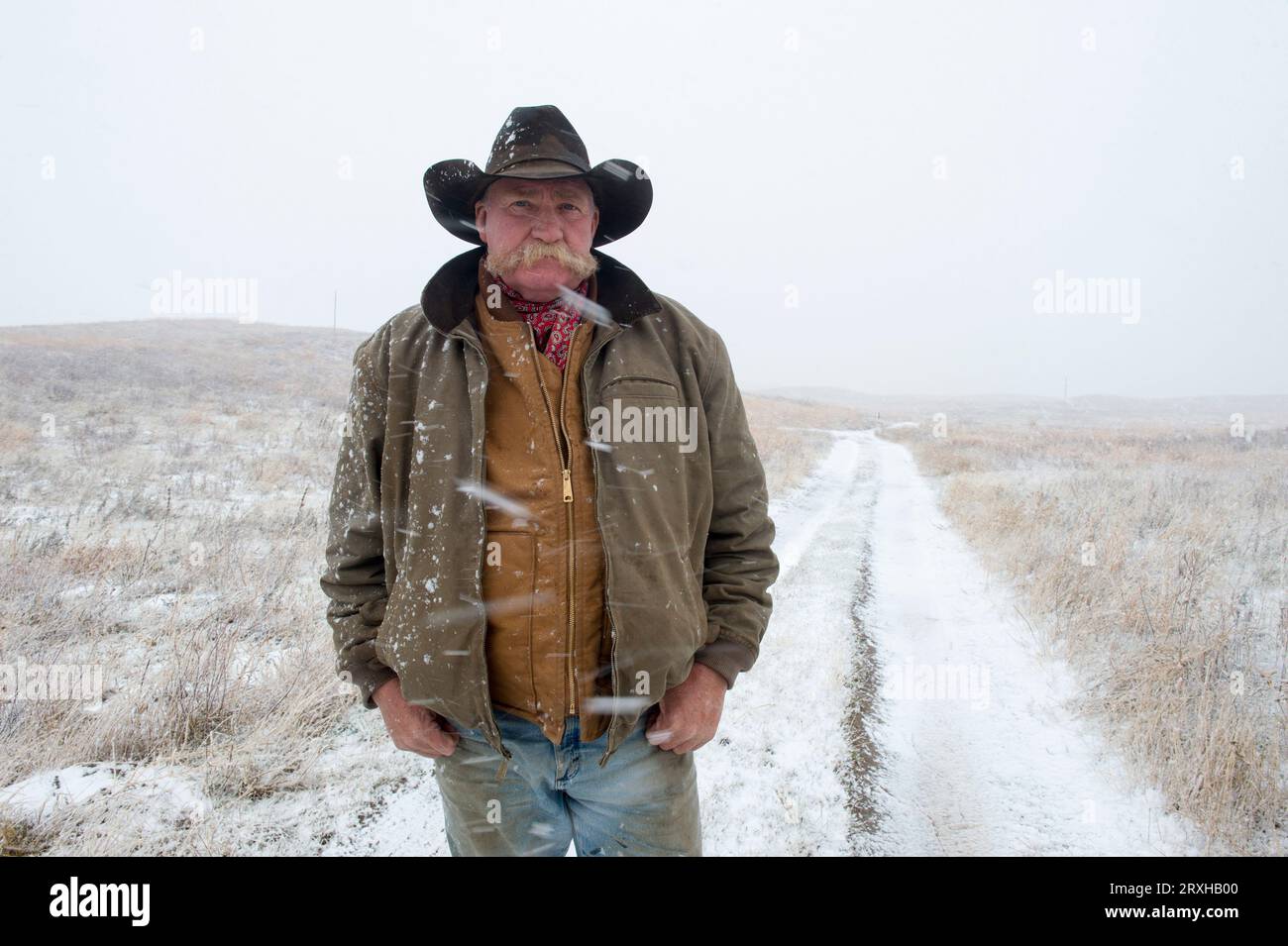 Outdoor portrait of a man in a cowboy hat standing on a dirt road during a snow storm; Burwell, Nebraska, United States of America Stock Photo