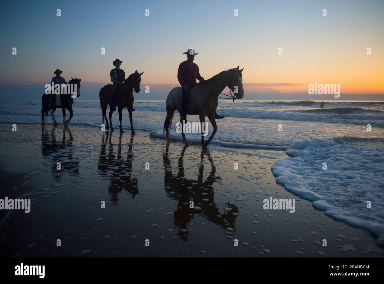 Cowboys ride their horses at sunrise along Virginia Beach in First