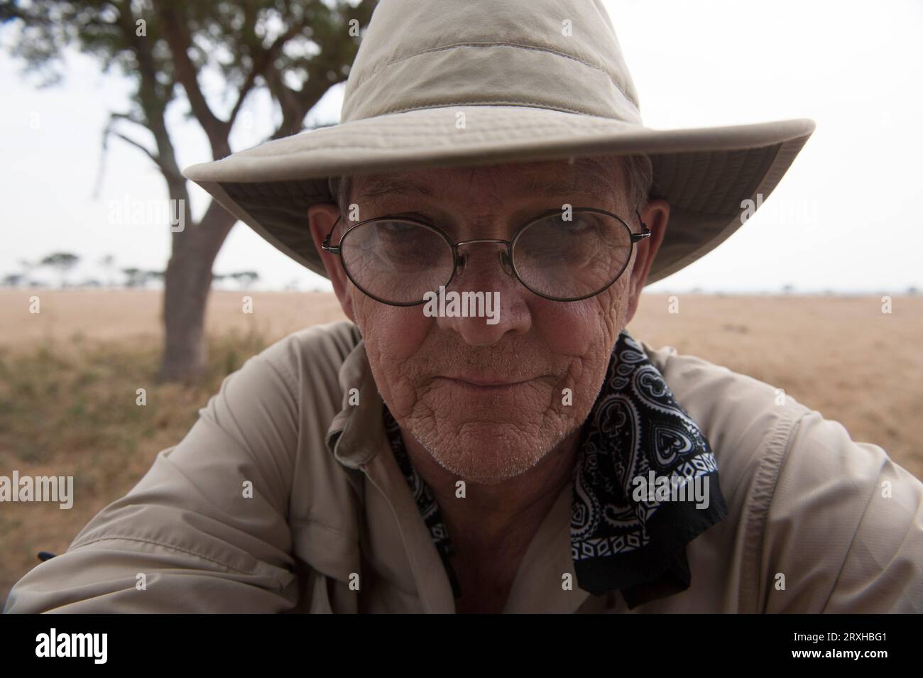 Close-up portrait of a man outdoors in Queen Elizabeth National Park, wearing a hat, bandana and eyeglasses; Uganda Stock Photo