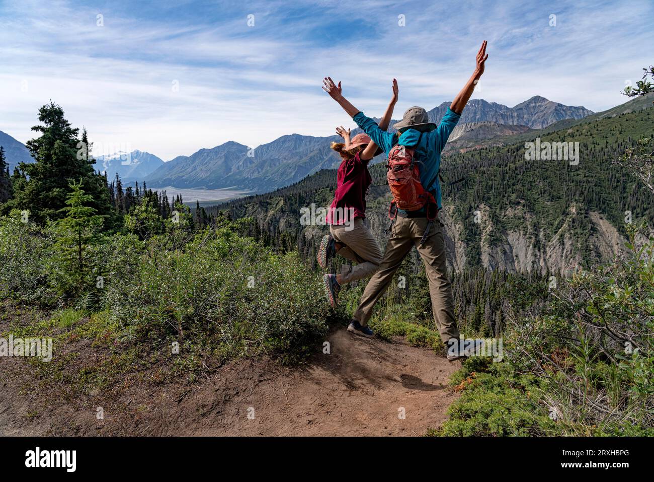 Two people on a mountaintop jumping up with their hands raised and having a good time during a hike in the Yukon wilderness; Yukon, Canada Stock Photo