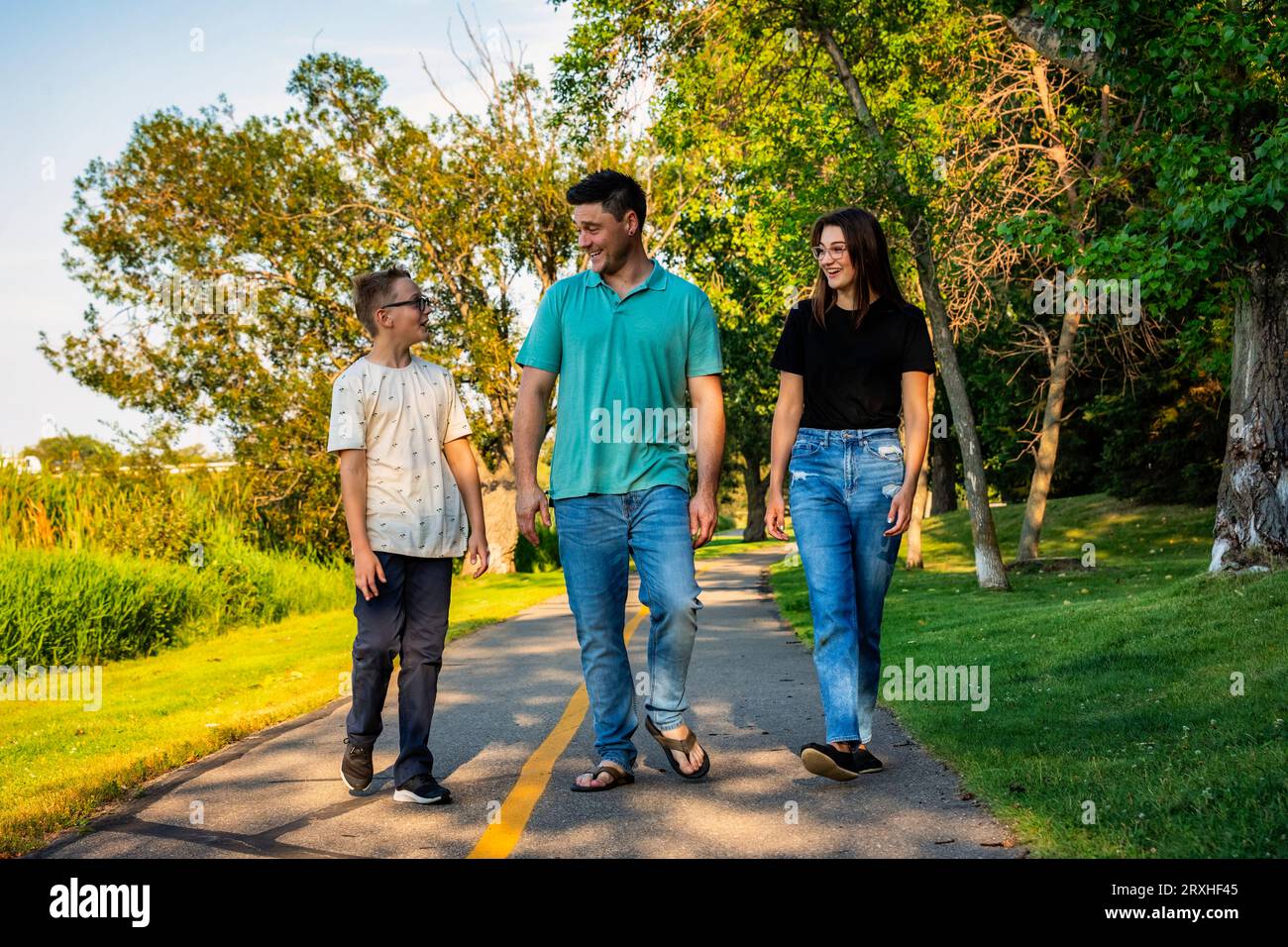 Father spending quality time outdoors with his teenage children, walking and talking in a city park during a warm fall afternoon Stock Photo