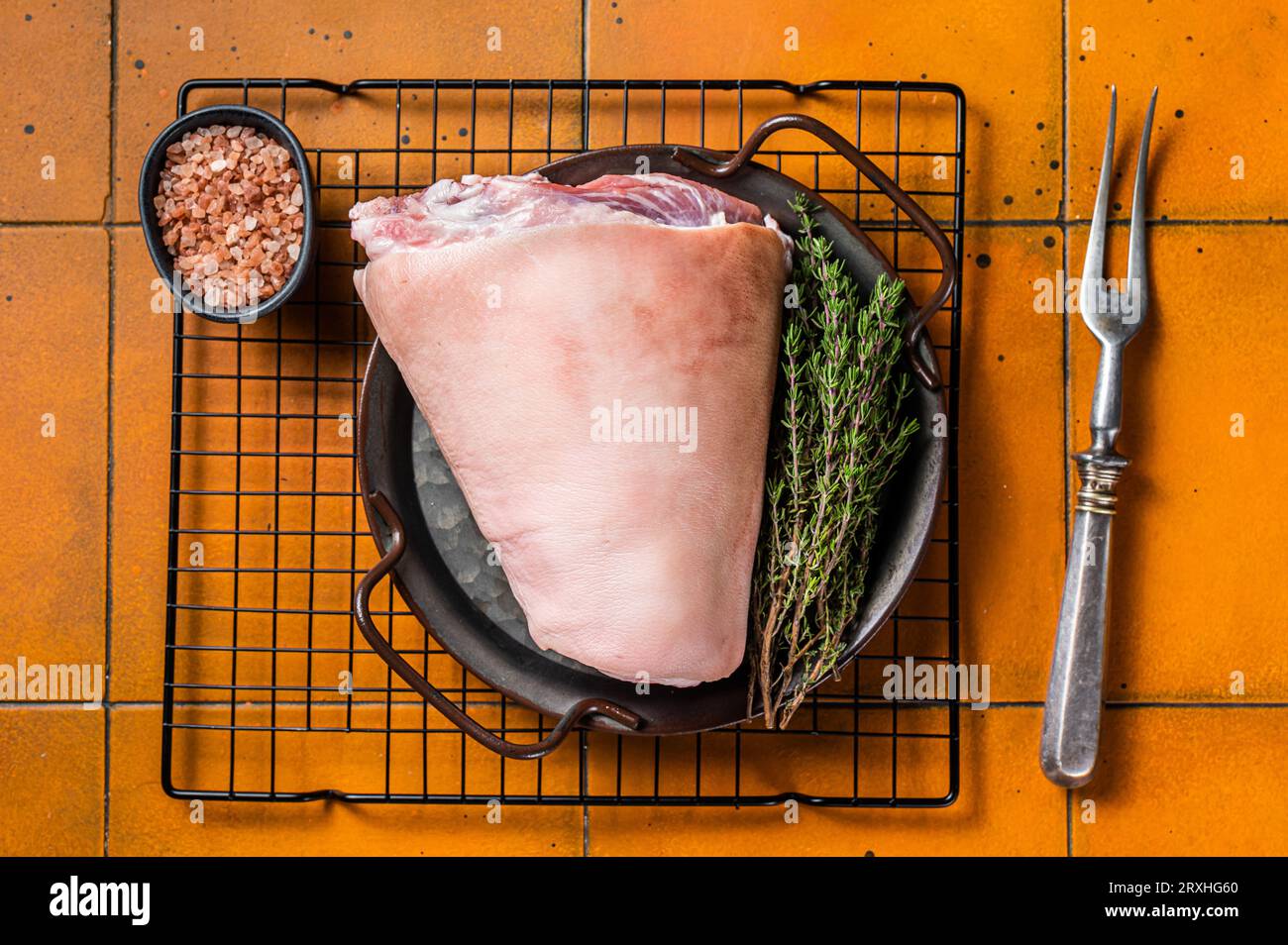 Raw pork shank knuckle in a steel tray with herbs. Orange background