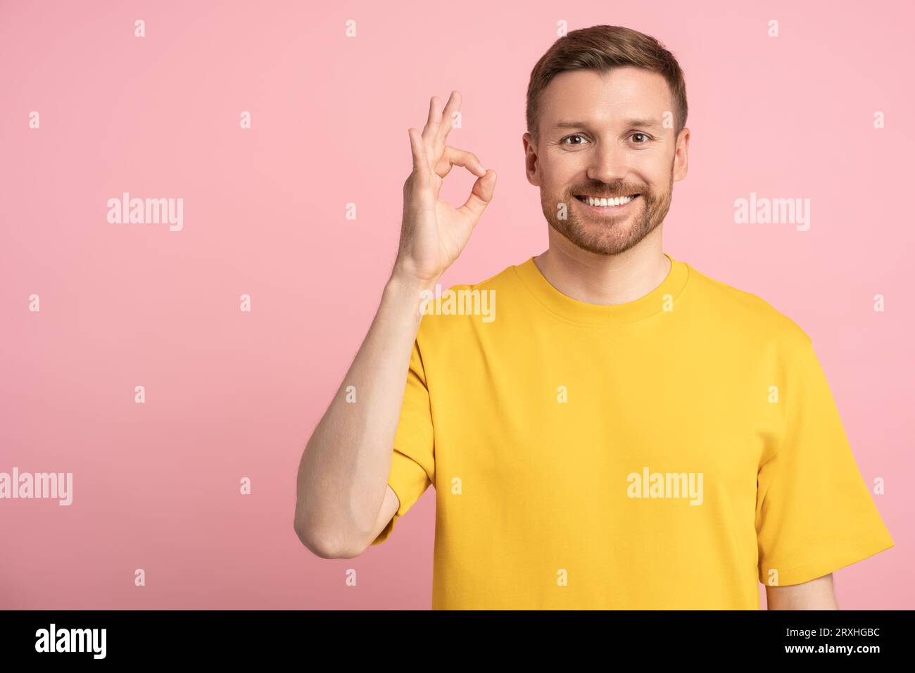Positive happy man showing OK sign hand gesture on pink background looking at camera. Stock Photo