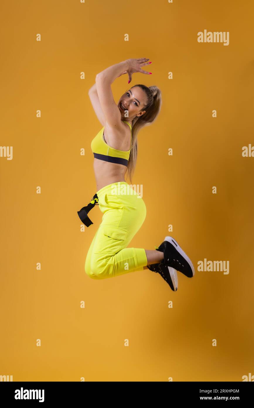 Beautiful happy girl in yellow outfit jumping against dark yellow or ...