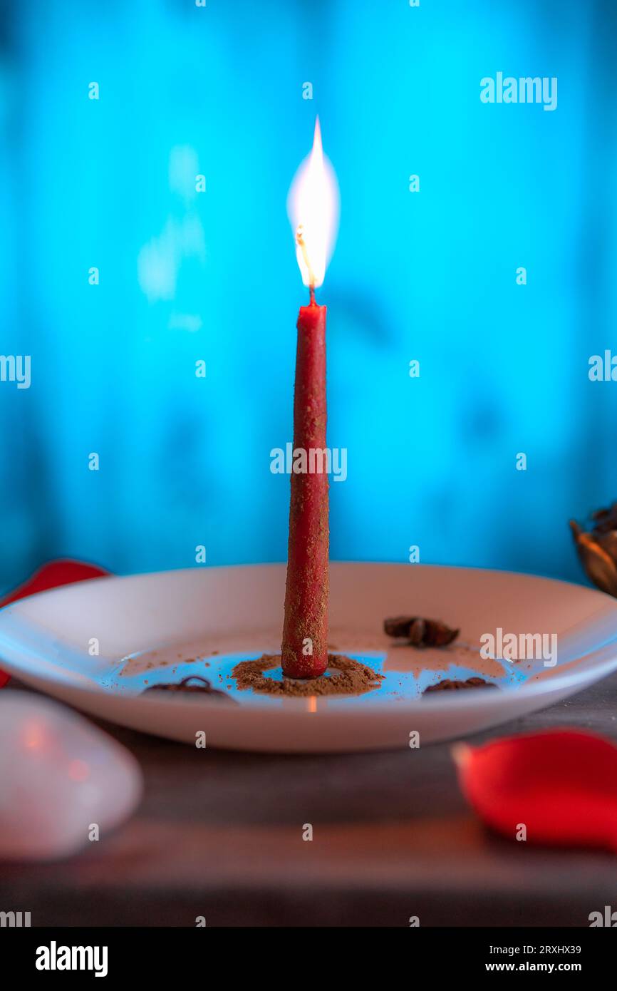 A red candle lit on a blue background, prepared with ground cinnamon with incense and rose quartz, copy paste , Halloween, spiritual beliefs, white ma Stock Photo