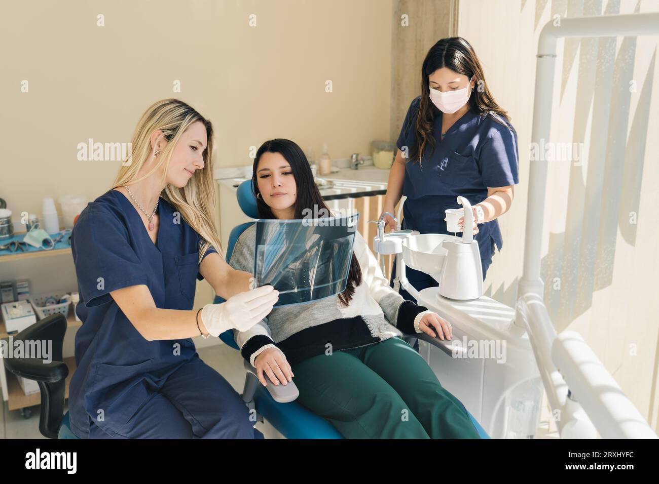 Latina female dentist explaining Tooth XRays To A Patient, while her assistant pours water for