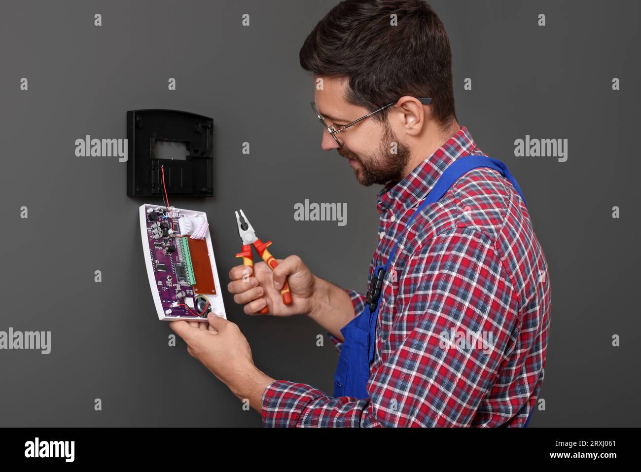 Technician installing home security alarm system on gray wall indoors