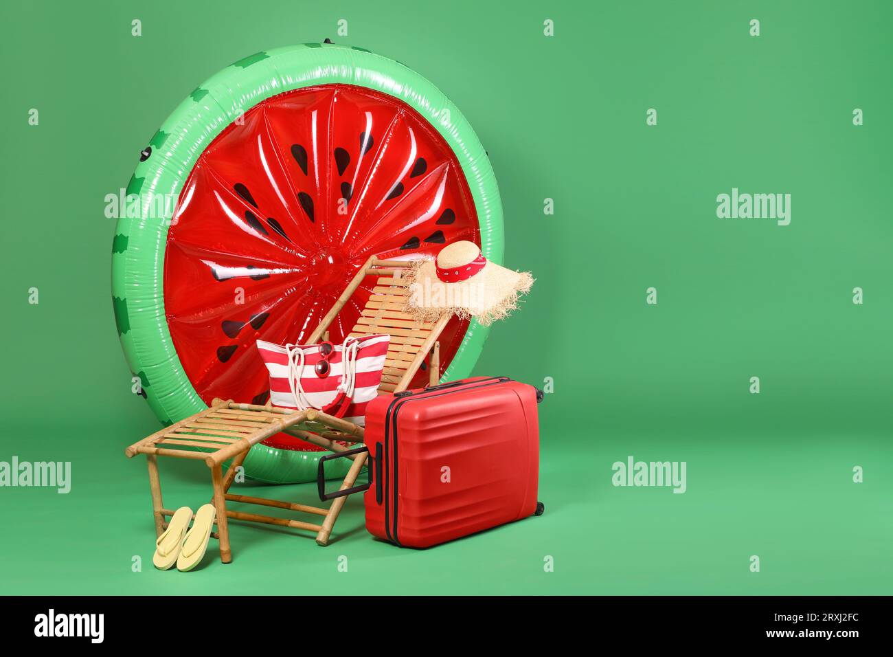 Deck chair, suitcase and beach accessories on green background, space for text Stock Photo