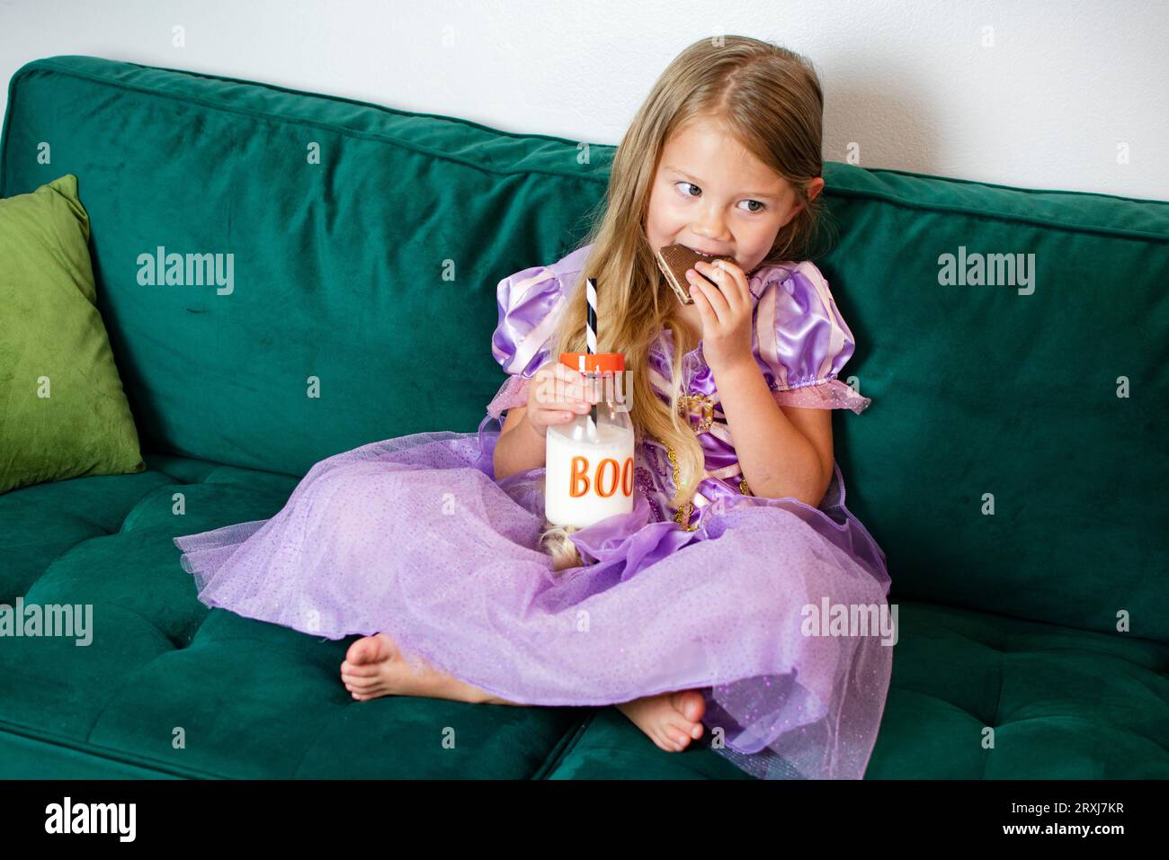 Cute Caucasian little girl is eating cookie in a Halloween costume. Girl in purple dress. Kids and Halloween concept Stock Photo