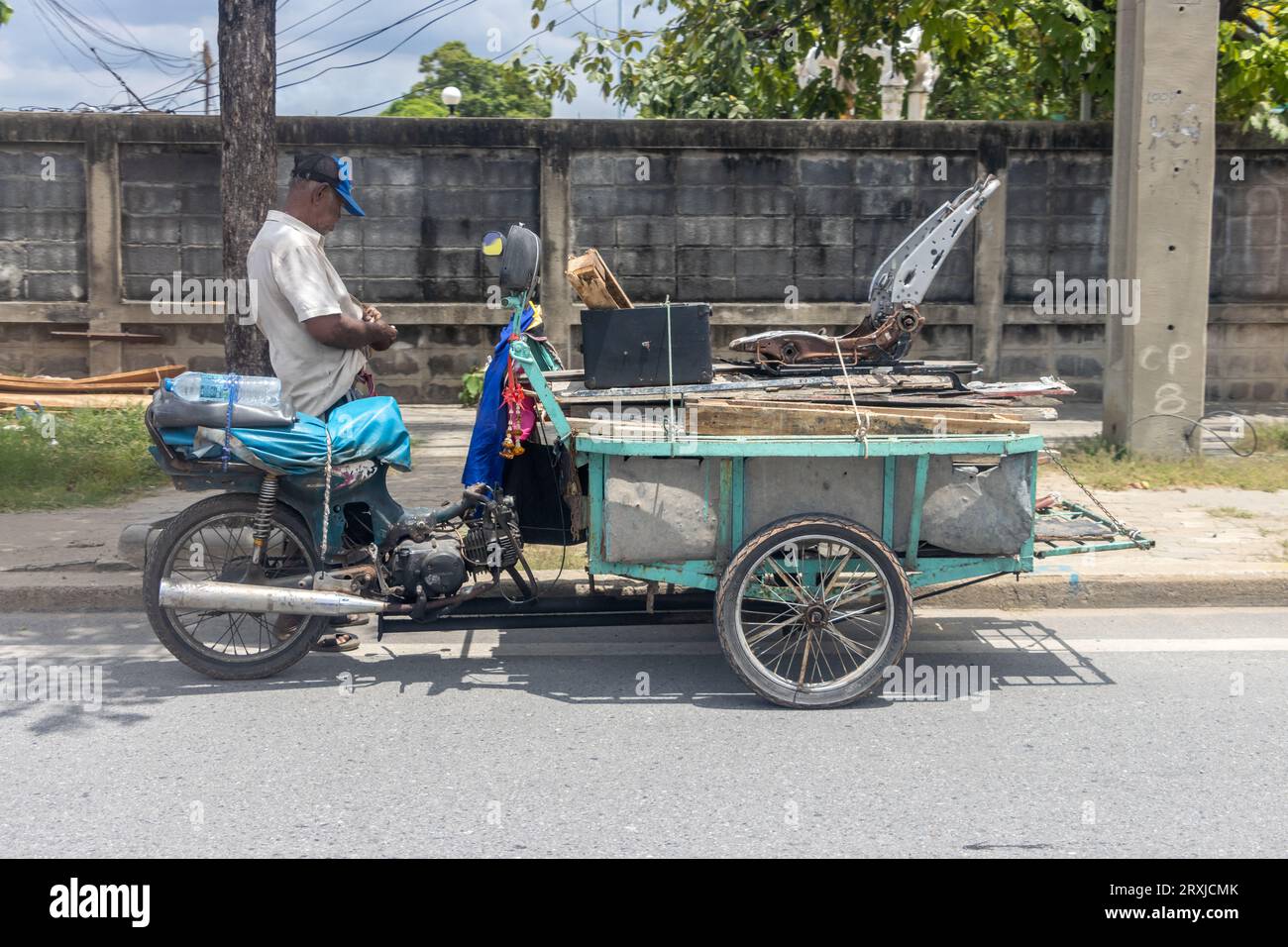 SAMUT PRAKAN, THAILAND, SEP 19 2023, A man with a tricycle loaded with used planks parks on the street Stock Photo