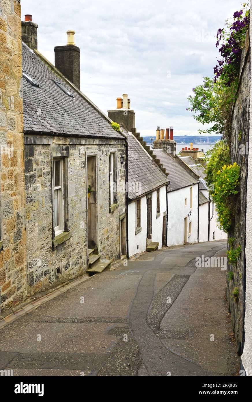 Quaint stone cottages line a narrow cobblestone street in the village of Culross, Scotland. Just visible in the distance is the Firth of Forth. Stock Photo