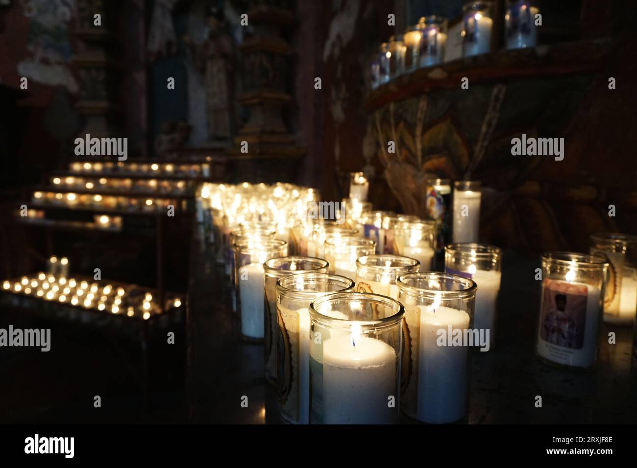 Lighted votive candles inside the San Xavier del Bac Mission near Tucson, Arizona. Some of the Mission's carved and painted decor is visible behind Stock Photo