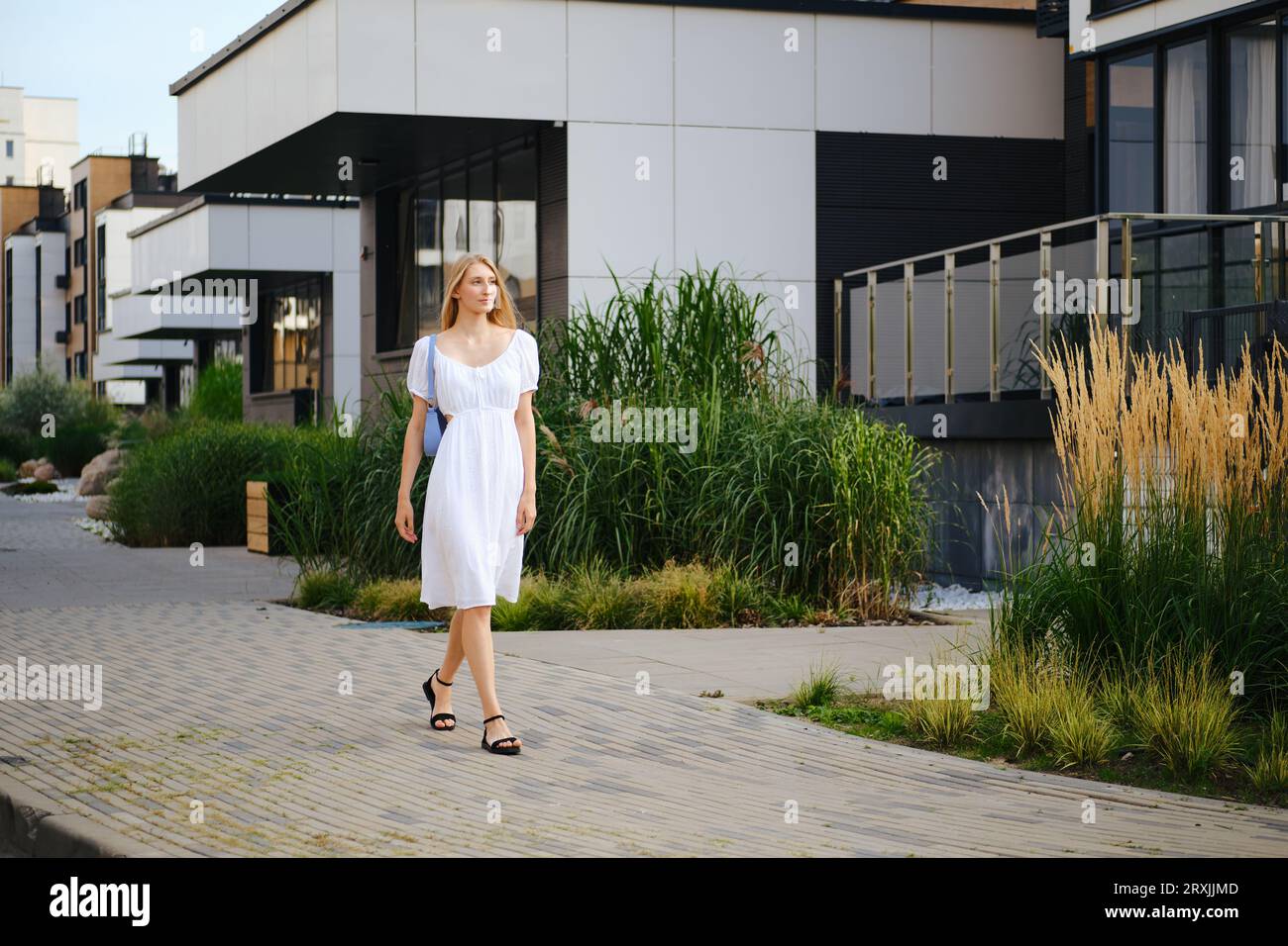 Blonde woman walking along the pavement in modern residential area Stock Photo