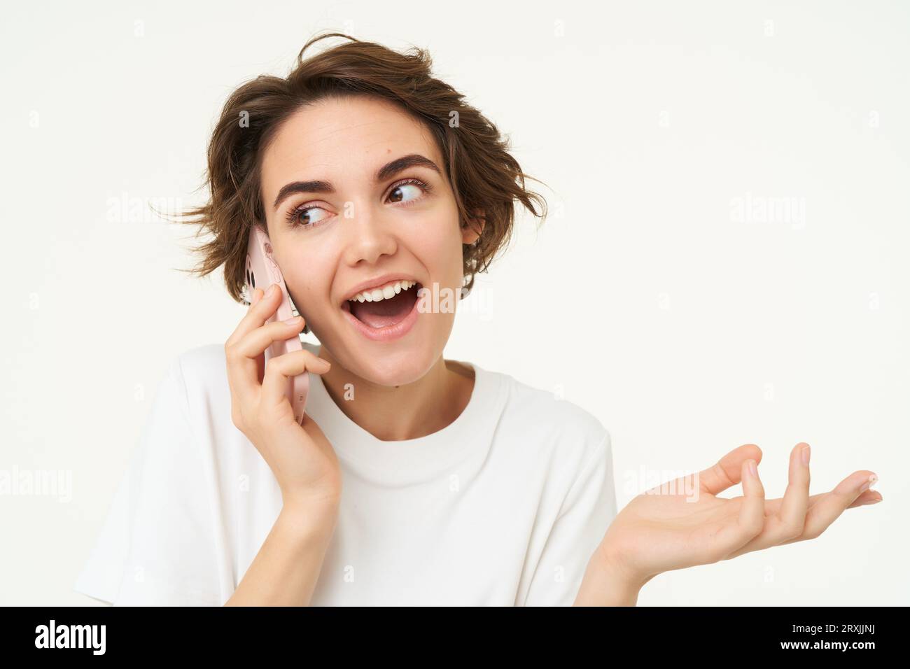 Portrait of happy, chatty young woman talking on mobile phone, using smartphone, calling someone, standing over white studio background Stock Photo