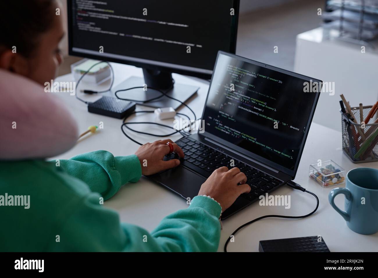 Programmer sitting at her workplace with computers and writing codes on laptop in office Stock Photo