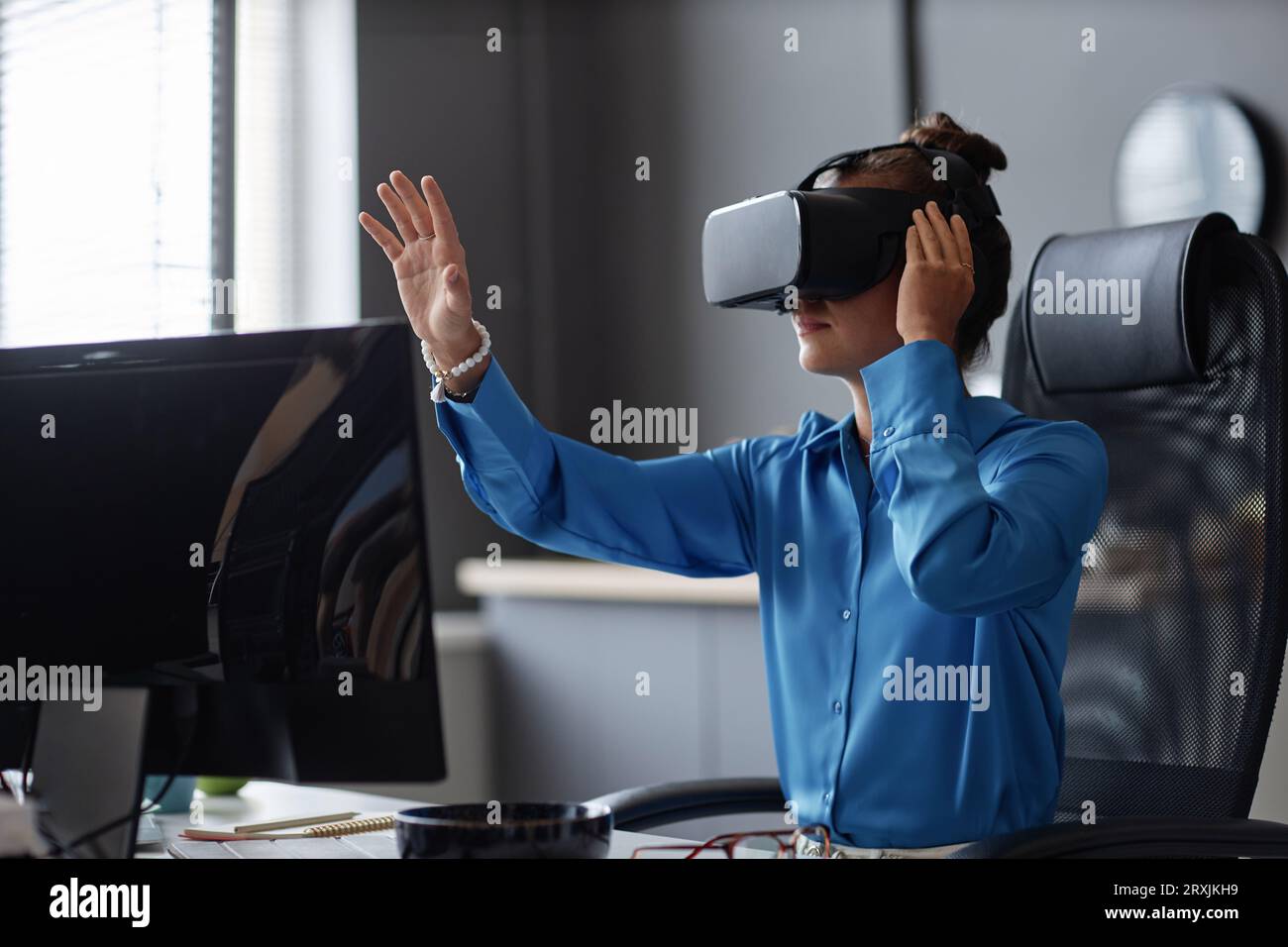 Young woman testing new program in VR glasses while sitting at her workplace Stock Photo
