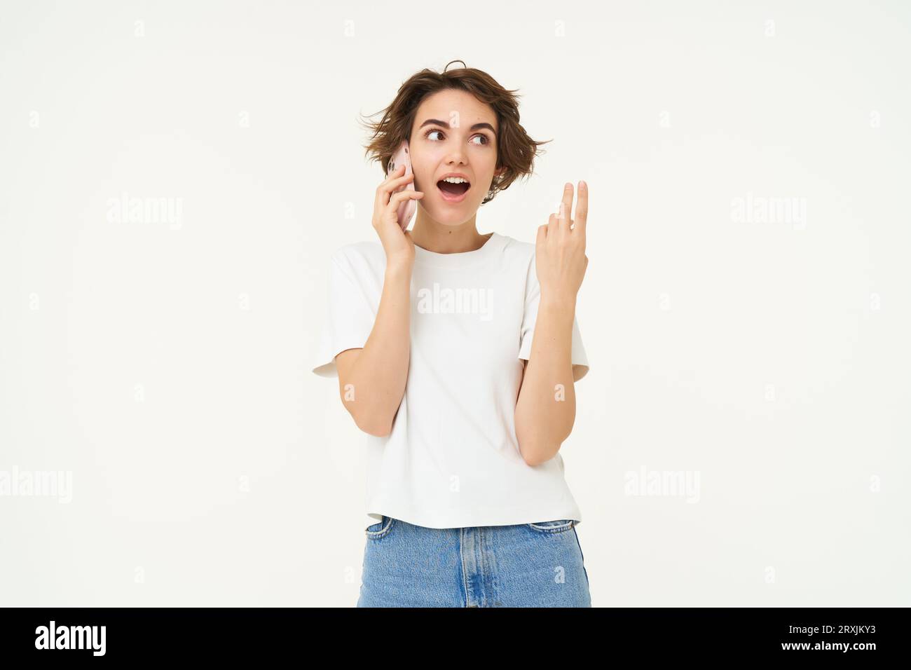 Portrait of chatty young woman, talking on mobile phone and gesturing, discussing something over the telephone conversation, standing over white Stock Photo