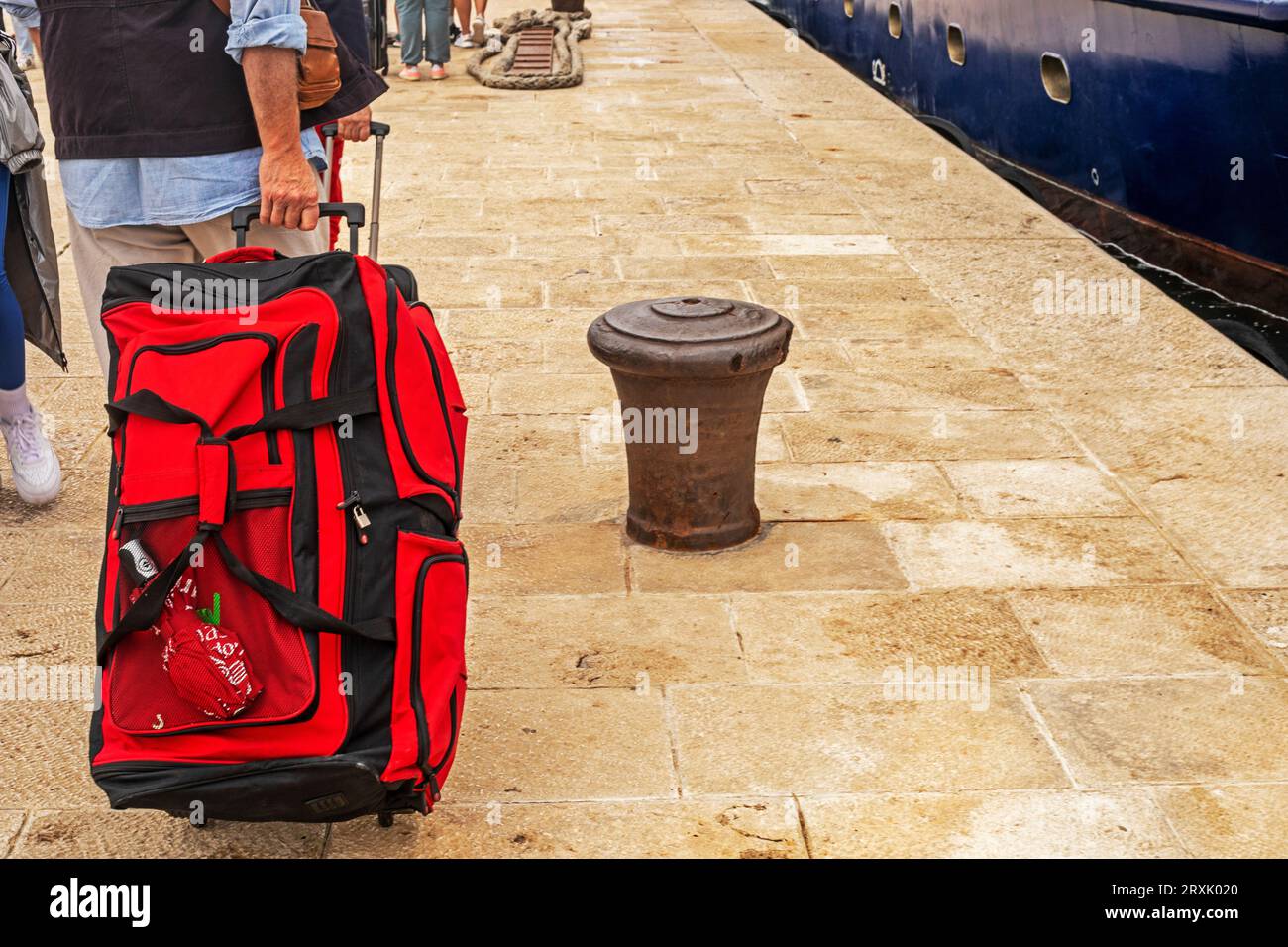 passenger's hands carry his red luggage on wheels on the pier on a