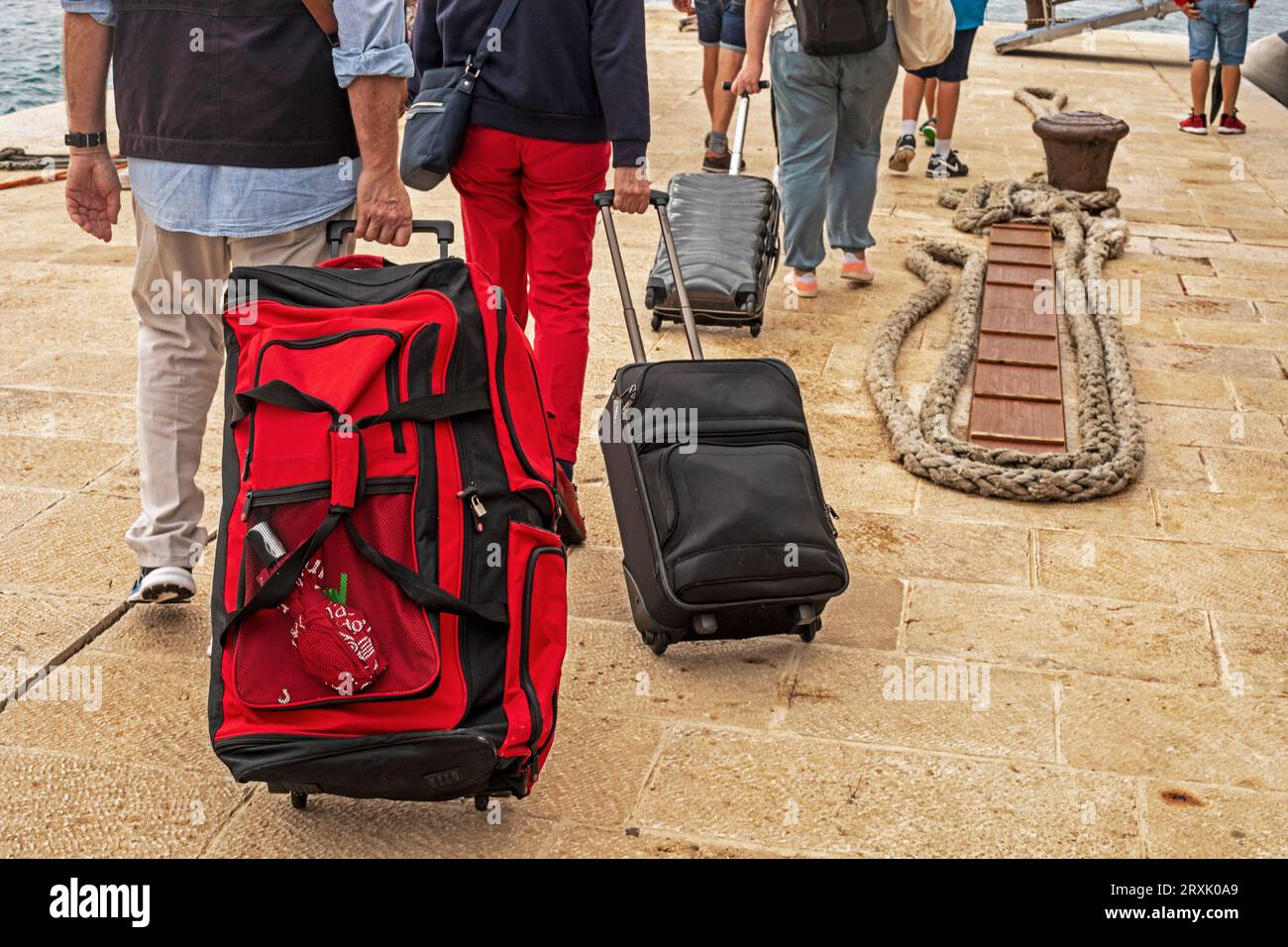 Passengers' hands carry their luggage on wheels on the pier on a sunny