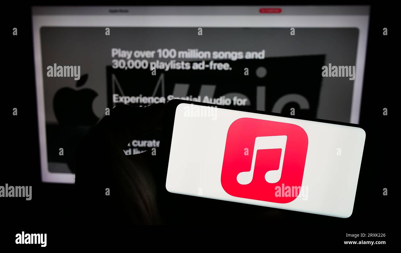 Person holding cellphone with logo of streaming service platform Apple Music on screen in front of business webpage. Focus on phone display. Stock Photo