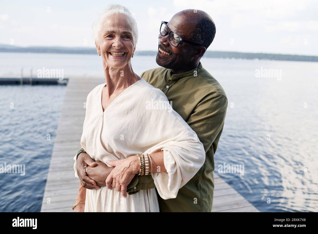 African American senior man embracing his happy wife while they standing on pier Stock Photo