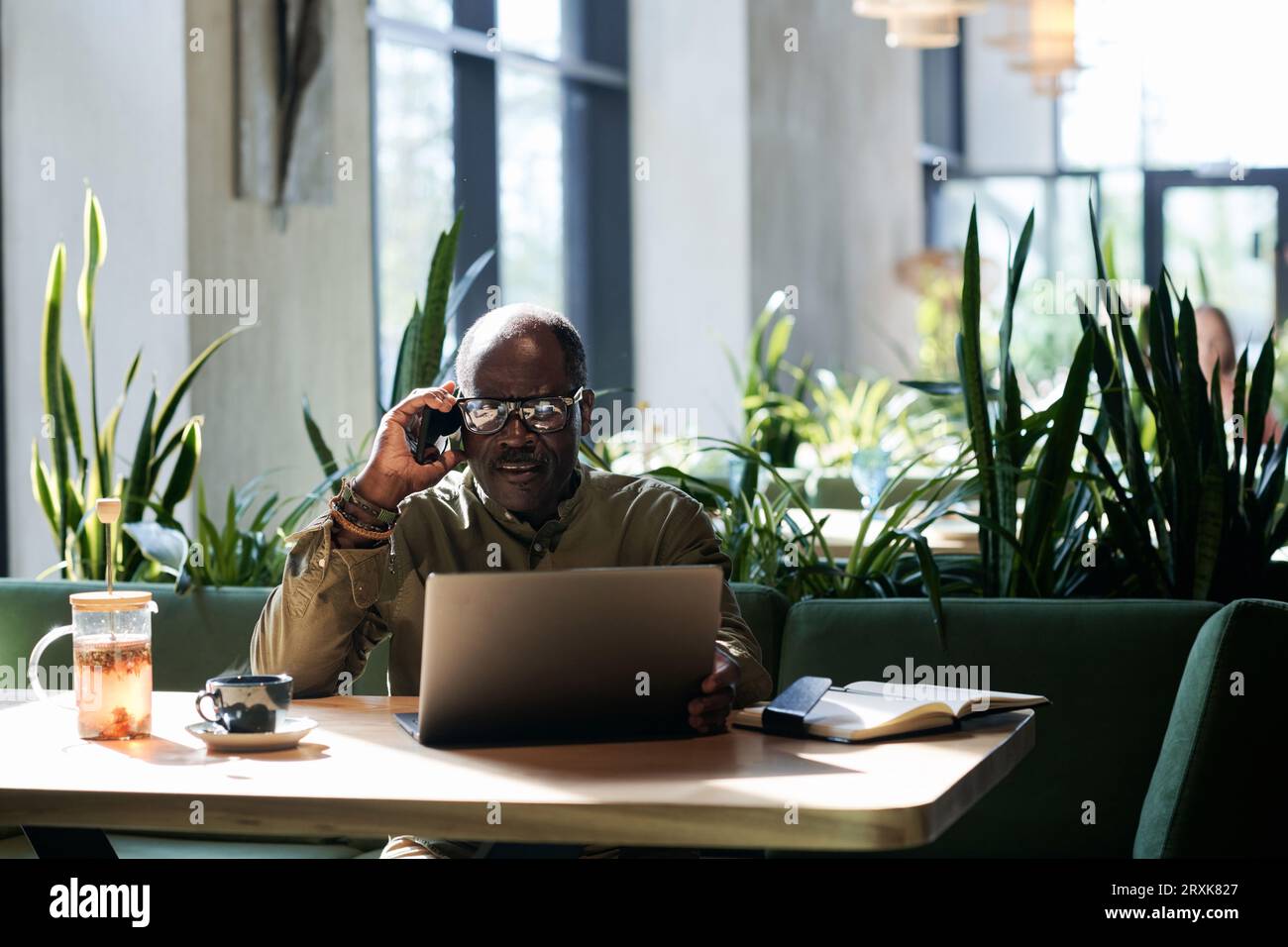 Senior man using laptop and talking on the phone while sitting in cafe Stock Photo