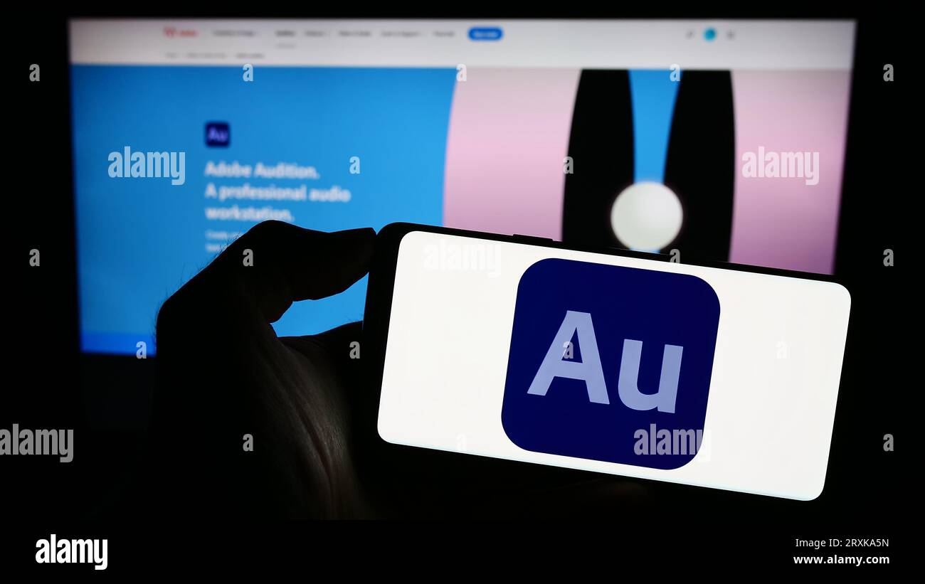 Person holding cellphoen with logo of digital audio workstation Adobe Audition on screen in front of business webpage. Focus on phone display. Stock Photo
