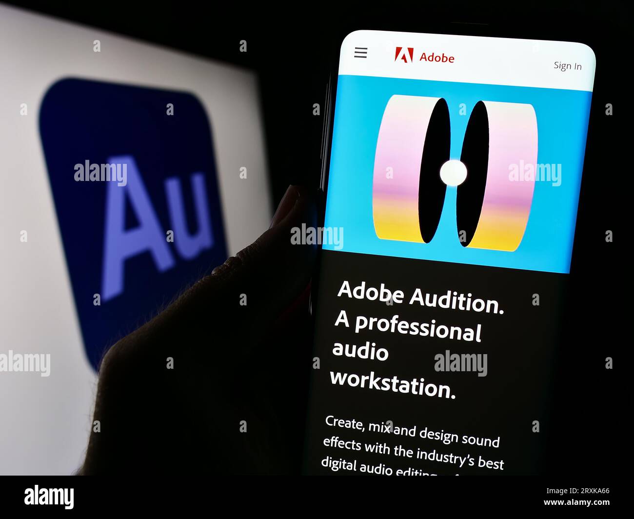 Person holding cellphone with webpage of digital audio workstation Adobe Audition on screen in front of logo. Focus on center of phone display. Stock Photo