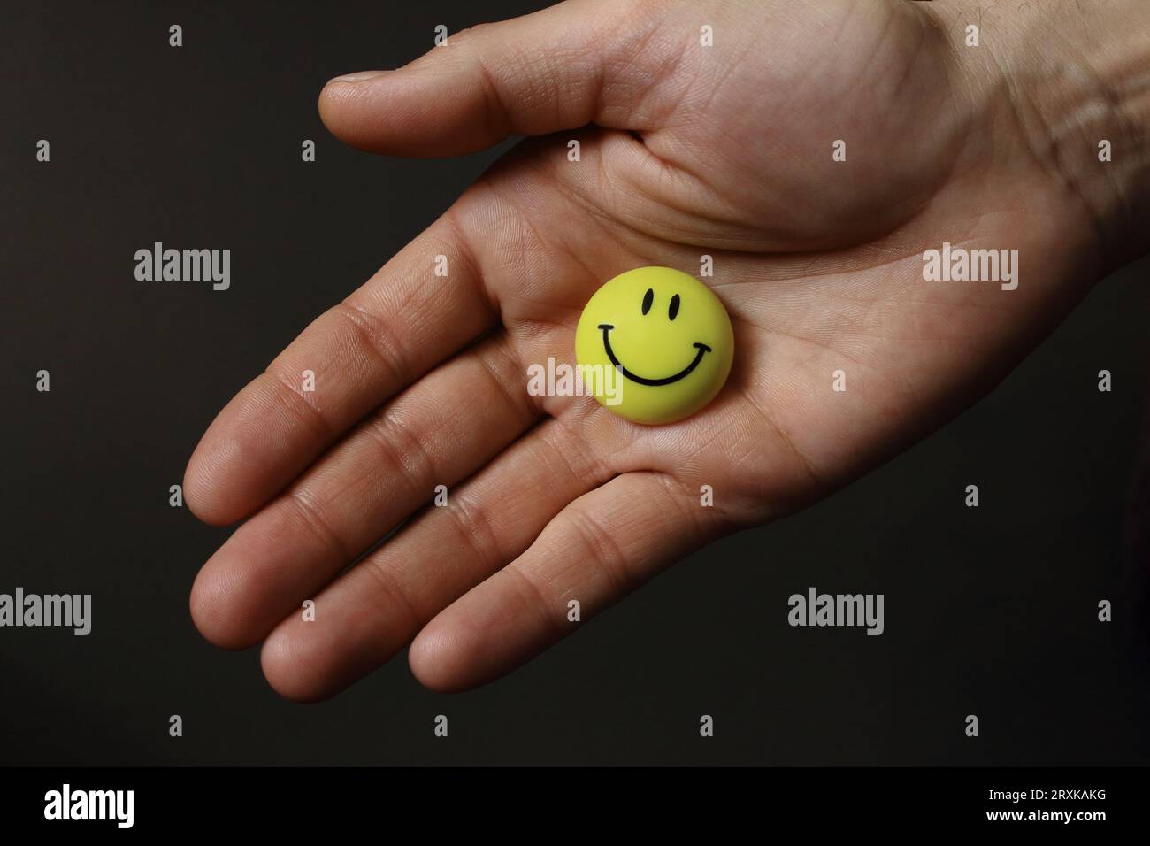 Yellow smiling face on open palm. Round smile face in open hand. Friendship Day concept. Cheerful emotions. Friendship proposal. Stock Photo